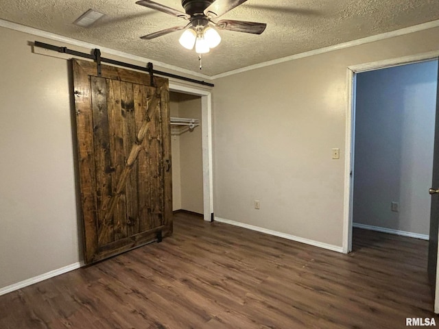 unfurnished bedroom featuring ceiling fan, dark hardwood / wood-style floors, crown molding, a barn door, and a textured ceiling