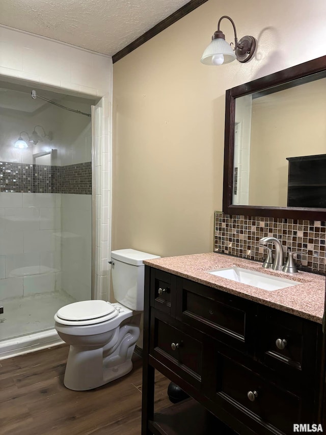 bathroom featuring toilet, hardwood / wood-style floors, vanity, backsplash, and tiled shower