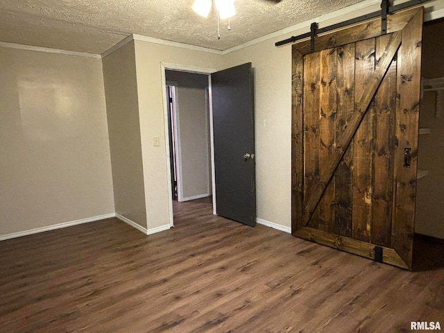 spare room featuring ceiling fan, dark hardwood / wood-style floors, crown molding, a barn door, and a textured ceiling