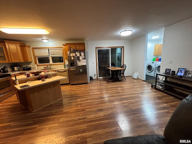 kitchen featuring kitchen peninsula, appliances with stainless steel finishes, washer and dryer, dark hardwood / wood-style floors, and sink