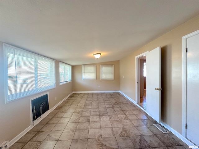 empty room featuring lofted ceiling, a baseboard heating unit, and light tile patterned flooring