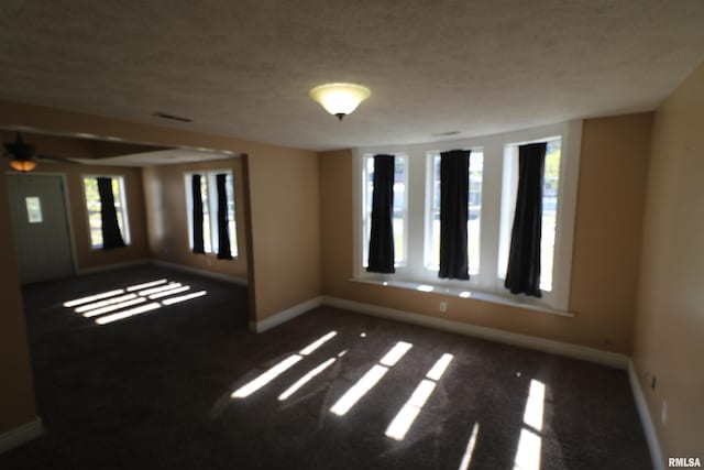 empty room featuring a textured ceiling and dark carpet