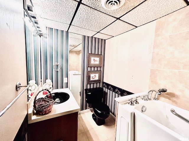 bathroom with vanity, a drop ceiling, toilet, and a bath