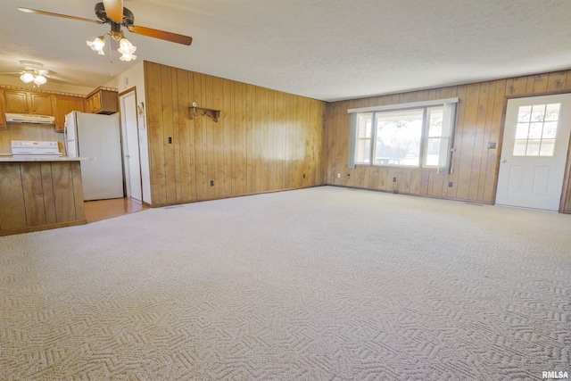 unfurnished living room with wooden walls, light carpet, and ceiling fan