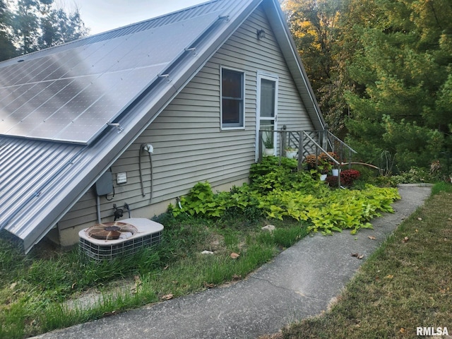 view of side of property featuring roof mounted solar panels, central AC unit, and metal roof