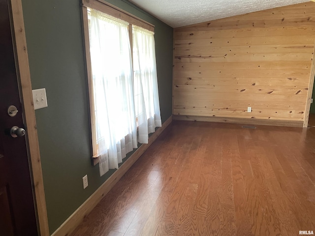 empty room featuring a textured ceiling, wood walls, hardwood / wood-style floors, and lofted ceiling