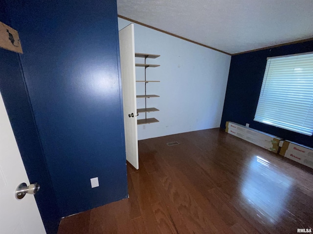 spare room featuring ornamental molding, lofted ceiling, a textured ceiling, and dark wood-type flooring