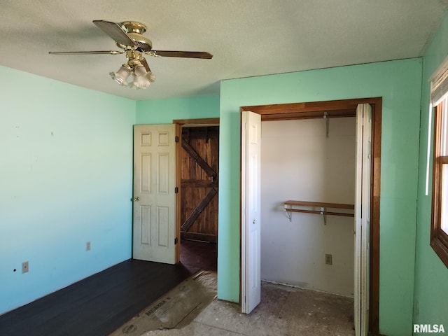 unfurnished bedroom featuring a textured ceiling, a barn door, a closet, and ceiling fan