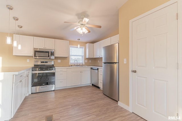 kitchen with hanging light fixtures, sink, white cabinets, light wood-type flooring, and appliances with stainless steel finishes