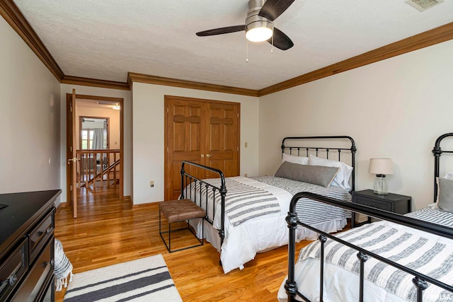 bedroom with a closet, crown molding, light wood-type flooring, a textured ceiling, and ceiling fan