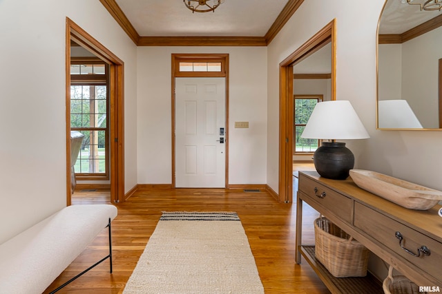 foyer featuring a healthy amount of sunlight, ornamental molding, and light wood-type flooring