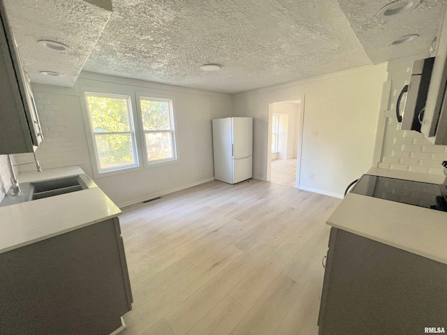 kitchen featuring stove, white refrigerator, sink, a textured ceiling, and light hardwood / wood-style floors