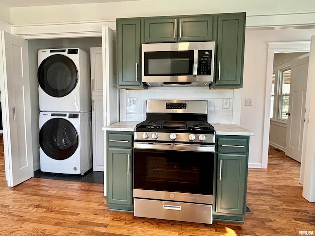 kitchen with green cabinetry, appliances with stainless steel finishes, stacked washer and clothes dryer, and light hardwood / wood-style floors