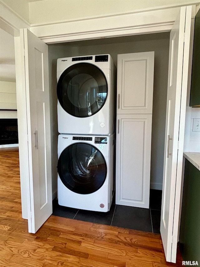 washroom with stacked washing maching and dryer, wood-type flooring, and cabinets