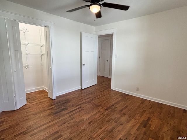 unfurnished bedroom featuring a spacious closet, a closet, ceiling fan, and dark hardwood / wood-style flooring