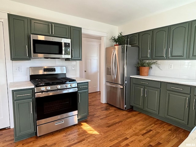 kitchen with hardwood / wood-style floors, appliances with stainless steel finishes, green cabinets, and backsplash