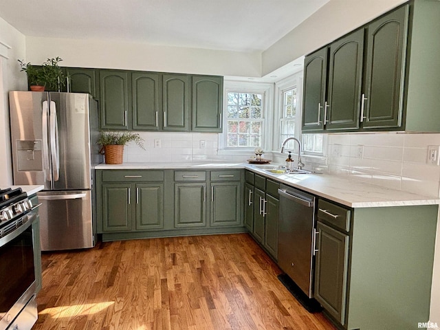 kitchen featuring stainless steel appliances, green cabinets, wood finished floors, and light countertops