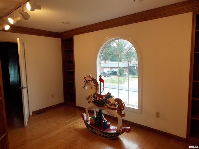 hall featuring light hardwood / wood-style floors, crown molding, and rail lighting