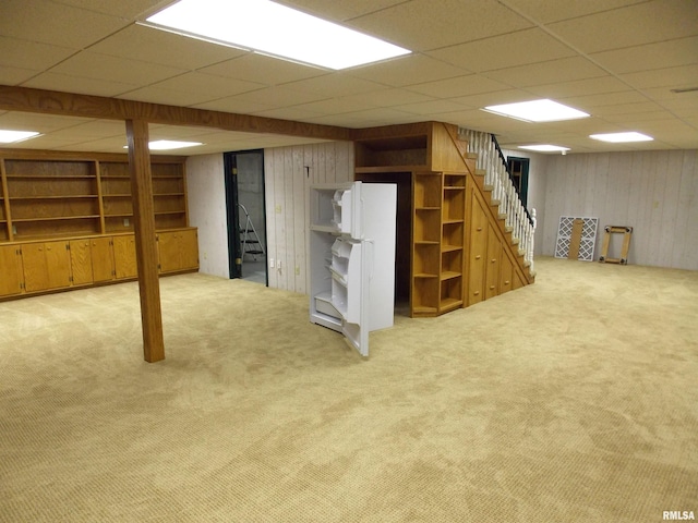 basement featuring a drop ceiling, light colored carpet, and wooden walls