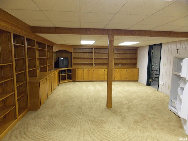 basement featuring light carpet, a paneled ceiling, and wooden walls