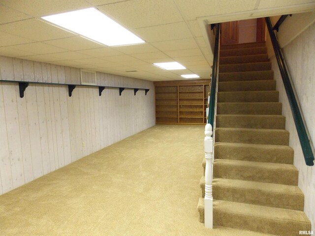 basement with a paneled ceiling, light carpet, and wooden walls