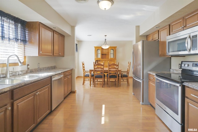 kitchen featuring appliances with stainless steel finishes, light hardwood / wood-style flooring, sink, and hanging light fixtures