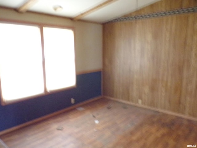 empty room featuring lofted ceiling, wooden walls, and wood-type flooring