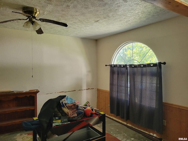 interior space featuring wooden walls, a textured ceiling, and ceiling fan