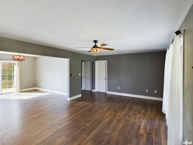 empty room featuring ceiling fan with notable chandelier and dark hardwood / wood-style floors