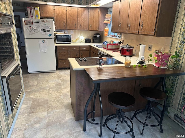 kitchen with tasteful backsplash, black electric cooktop, kitchen peninsula, a breakfast bar area, and white refrigerator