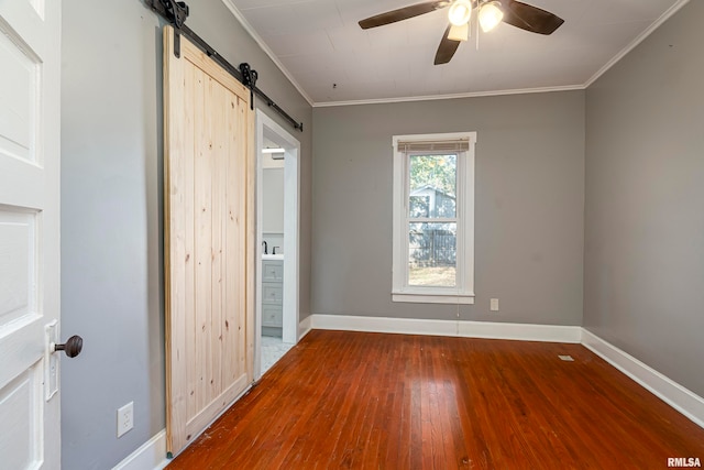 empty room featuring ornamental molding, a barn door, wood-type flooring, and ceiling fan