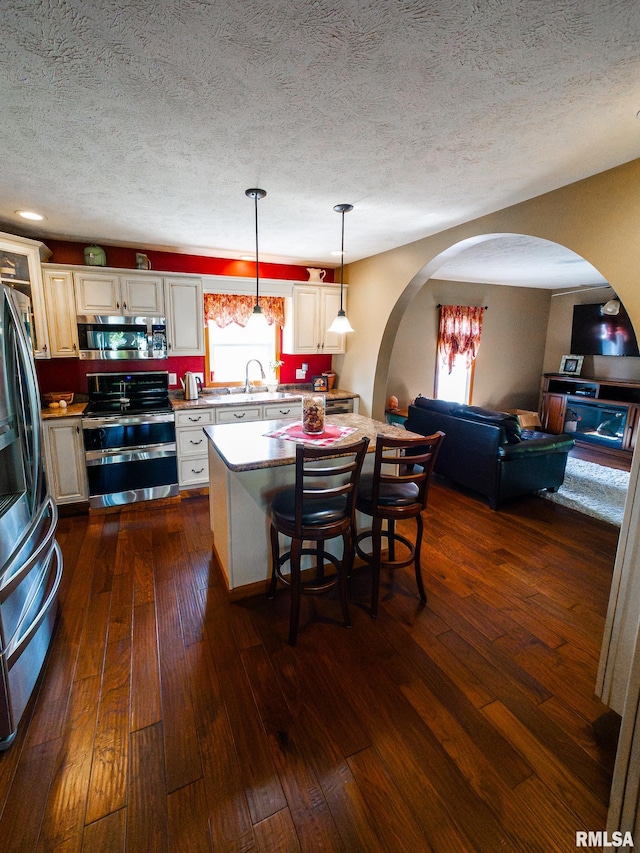 kitchen with a breakfast bar area, dark wood-type flooring, pendant lighting, appliances with stainless steel finishes, and a textured ceiling