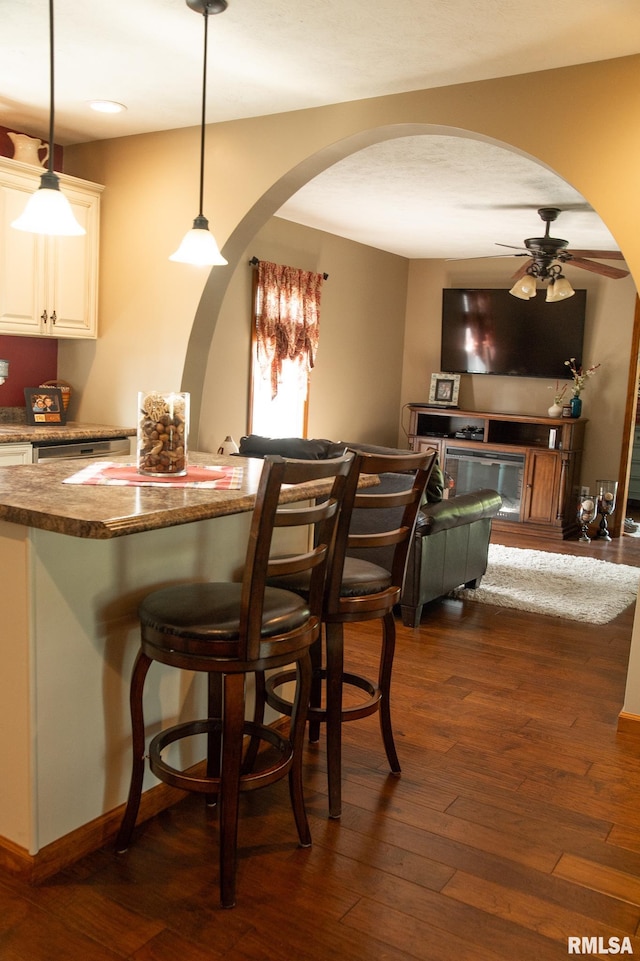 bar with dark wood-type flooring, white cabinets, decorative light fixtures, and dark stone countertops