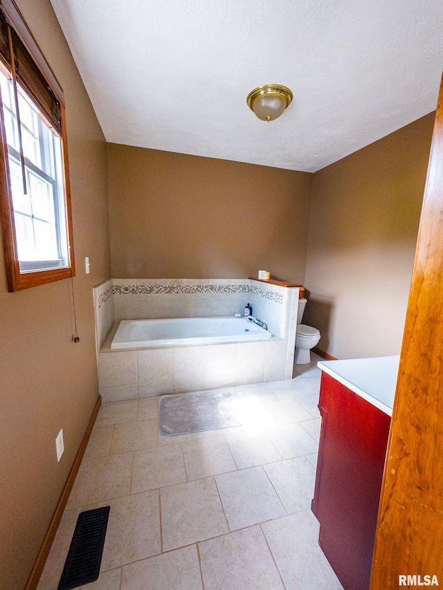 bathroom with toilet, tile patterned flooring, vanity, and tiled bath