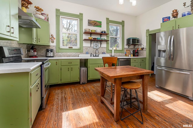 kitchen with dark hardwood / wood-style floors, wall chimney exhaust hood, green cabinets, appliances with stainless steel finishes, and tasteful backsplash