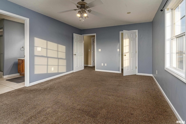 unfurnished bedroom featuring multiple windows, ceiling fan, light colored carpet, and ensuite bath