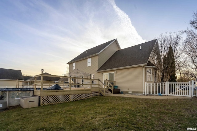 back house at dusk featuring a pool side deck and a yard