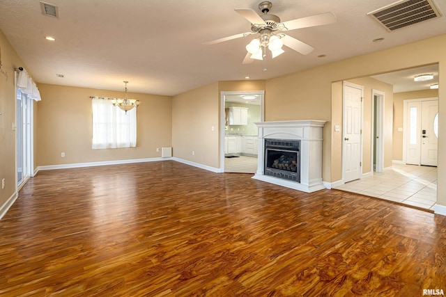 unfurnished living room featuring ceiling fan with notable chandelier and light wood-type flooring