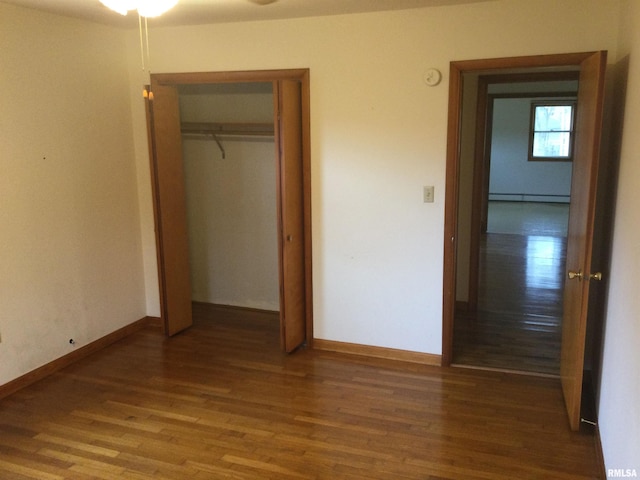 unfurnished bedroom featuring hardwood / wood-style floors, a baseboard heating unit, and a closet