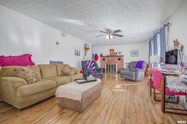 living room featuring ceiling fan, a brick fireplace, light hardwood / wood-style flooring, and a textured ceiling