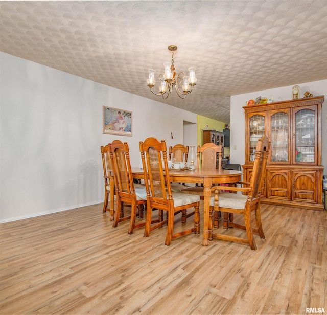 dining space with light wood-type flooring, an inviting chandelier, and a textured ceiling