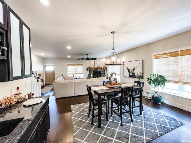 dining area featuring a fireplace, ceiling fan with notable chandelier, sink, and dark hardwood / wood-style flooring