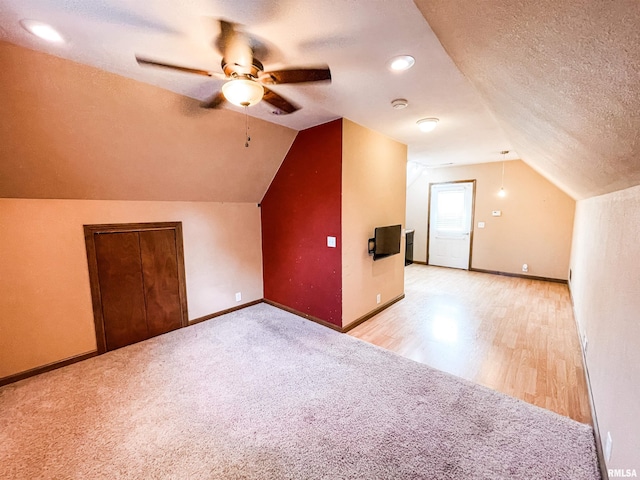 additional living space featuring ceiling fan, vaulted ceiling, light hardwood / wood-style floors, and a textured ceiling