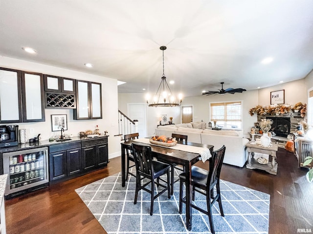 dining room featuring wine cooler, sink, dark hardwood / wood-style floors, ceiling fan with notable chandelier, and a fireplace