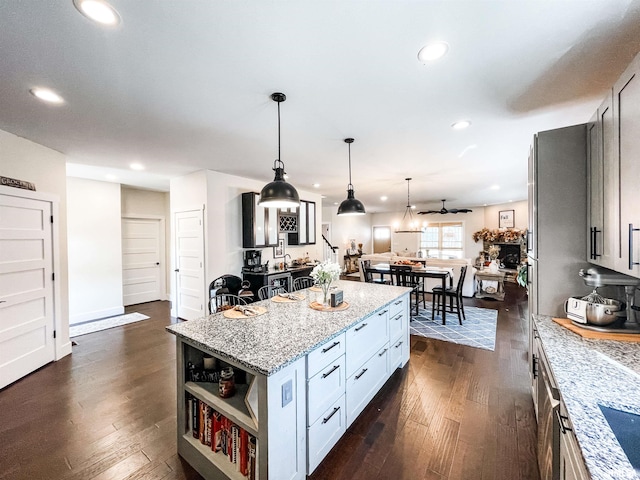 kitchen featuring dark hardwood / wood-style flooring, pendant lighting, light stone counters, and a center island