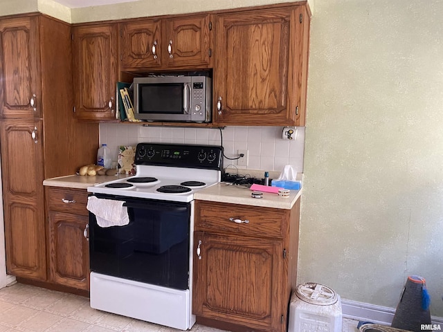 kitchen featuring brown cabinets, electric range, stainless steel microwave, backsplash, and light countertops