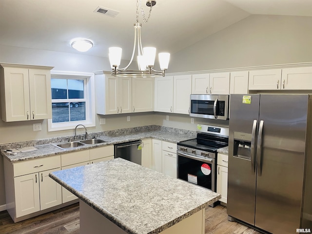 kitchen featuring appliances with stainless steel finishes, vaulted ceiling, a sink, and wood finished floors