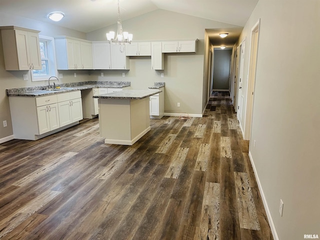 kitchen featuring dark wood-style flooring, a kitchen island, a sink, white cabinetry, and vaulted ceiling