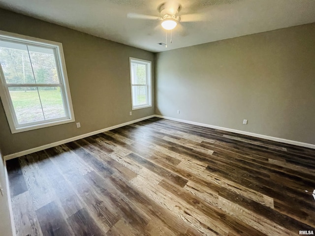 empty room featuring dark wood-type flooring, a ceiling fan, and baseboards