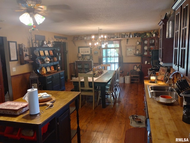 dining space featuring dark hardwood / wood-style flooring, a textured ceiling, wooden walls, sink, and a notable chandelier